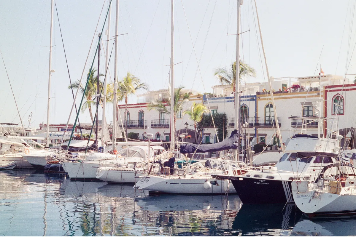 Sailing boats moored in Puerto de Mogán in front of whitewashed houses and palm trees