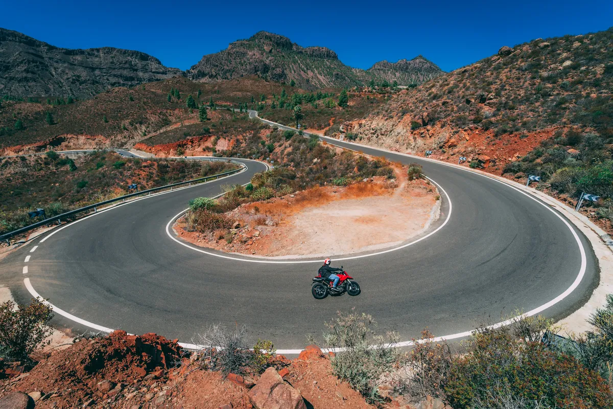 A hairpin bend on the mountain road to Fataga, with a motorcyclist and mountains behind
