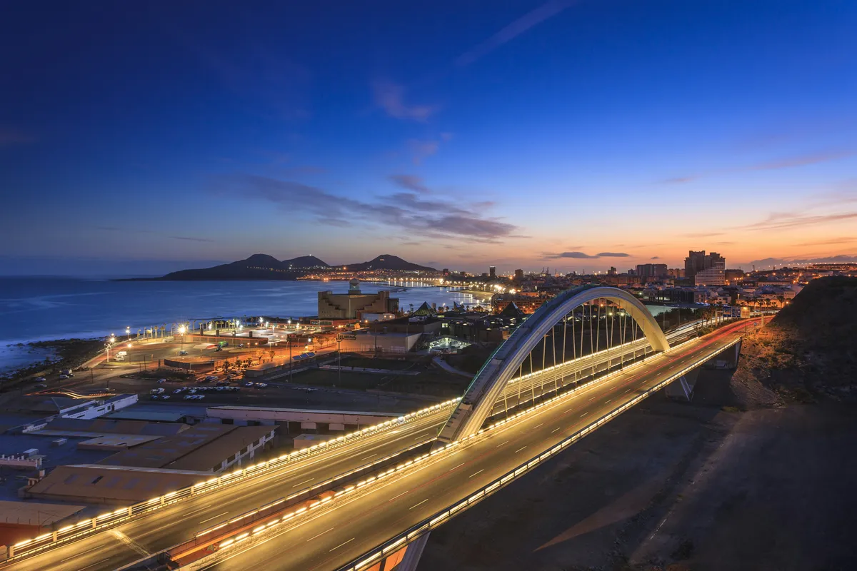 Las Palmas de Gran Canaria at dusk, with an illuminated bridge and the city by the sea