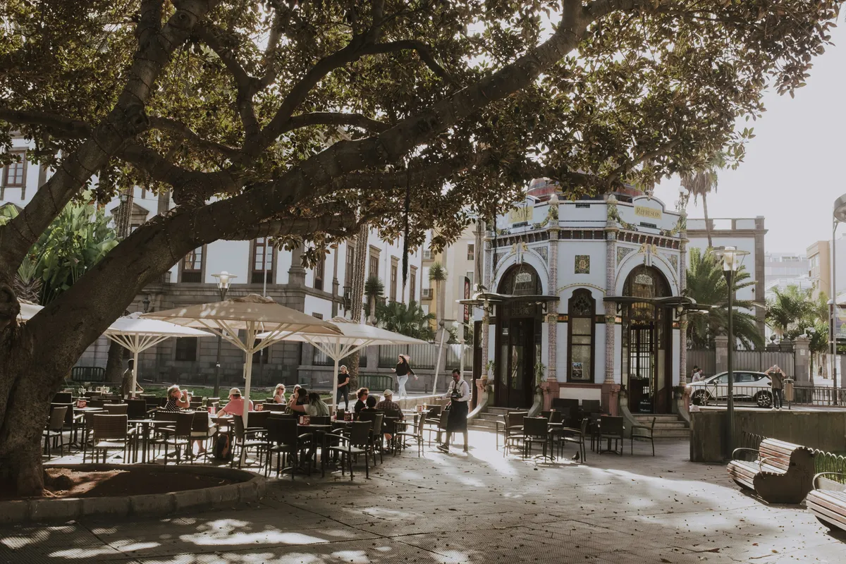 Café tables under a large tree beside the modernist kiosk in San Telmo park