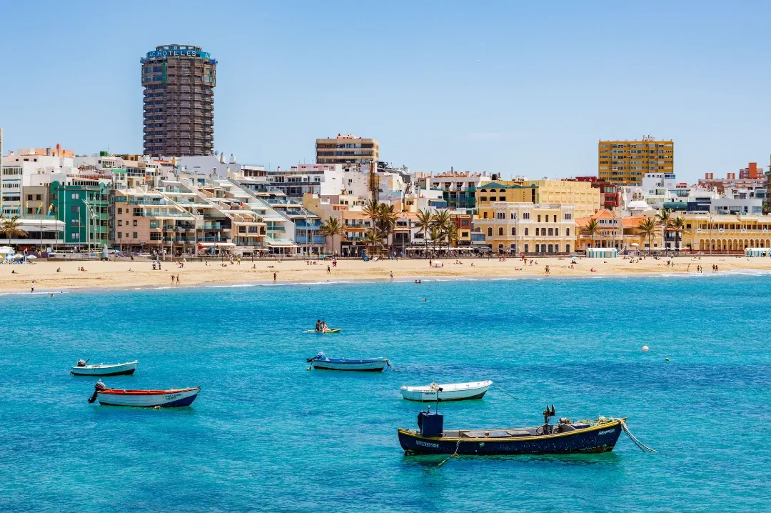 Small boats on turquoise water in front of a city beach in Las Palmas de Gran Canaria